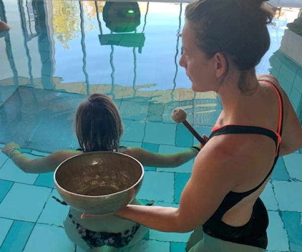 Une femme guide une enfant dans une séance de bols chantants dans une piscine.